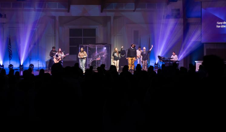 A group of people singing on a stage with a large crowd