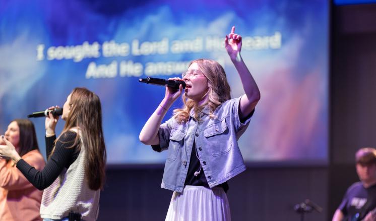 A group of people singing on a stage with large projector screens behind them