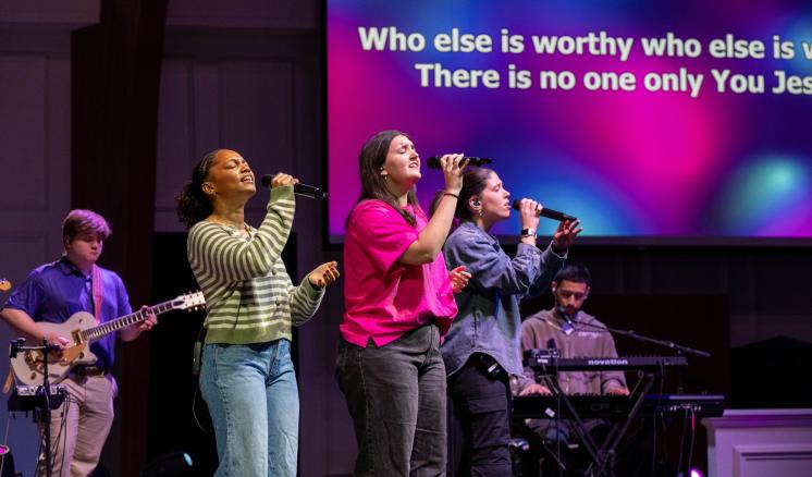 A group of people singing on a stage with large projector screens behind them