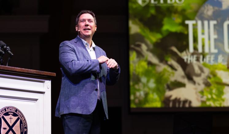 A amn stood on stage addressing an audience behind a podium