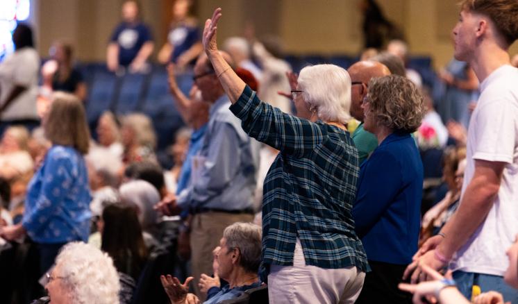 A group of people standing in an auditorium, some raising their hands.
