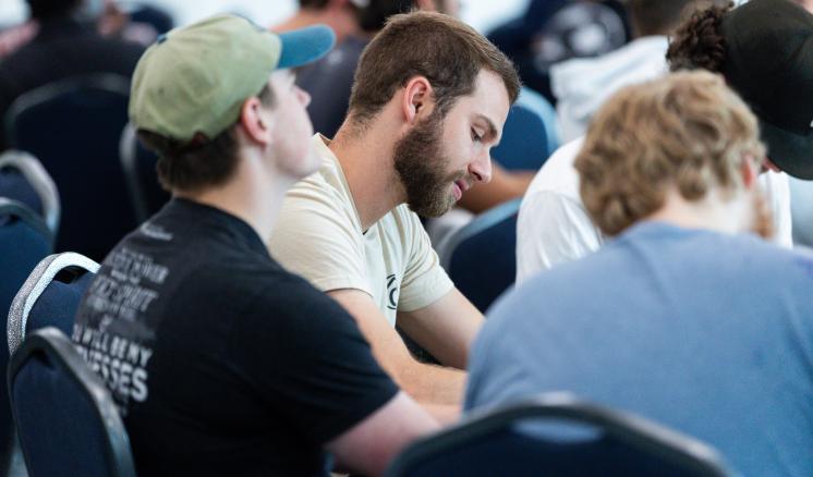 A man sits at a table with a group looking down at his notes