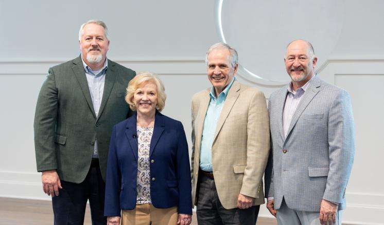 Four people stand together for a photo, each wearing a blazer and smiling