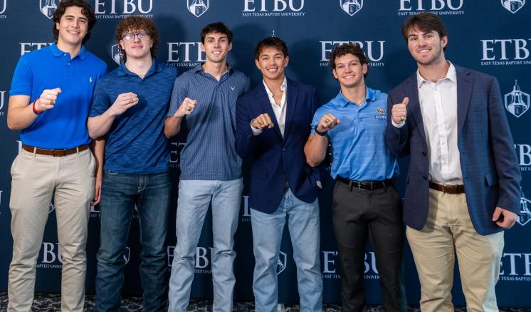 Six students stand in front of an ETBU-branded backdrop showing their class rings