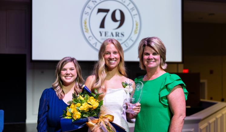 Senior Girl Call Out with her mother and sponsor smiling holding flowers and trophy.