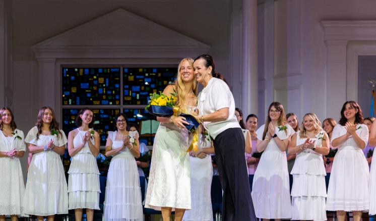 Senior Girl Call Out event at ETBU with girls on stage with a winner receiving flowers in the center getting a hug.