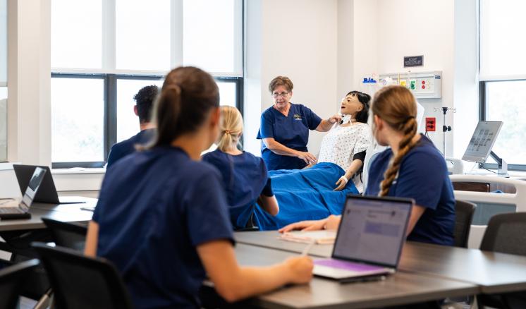 Nursing instructor with dummy teaches with students in the foreground.