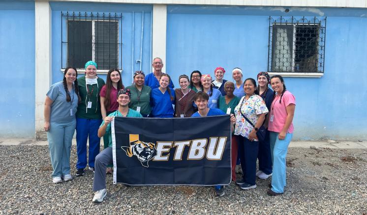 Group of people with an ETBU flag in front of a blue building.