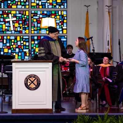 Student shakes hand of professor on stage and she receives a 2024 Academic Excellence Award