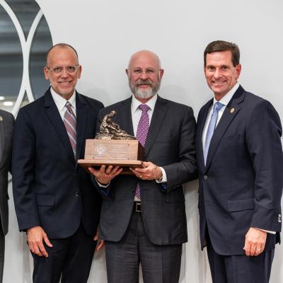 Four men in suits stand together, one holding a statue with a wooden base.