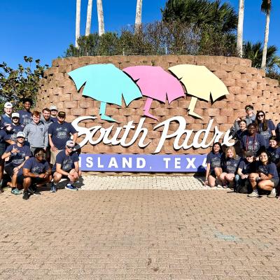 A group of people standing in front of a brick wall with South Padre Island Texas written on it