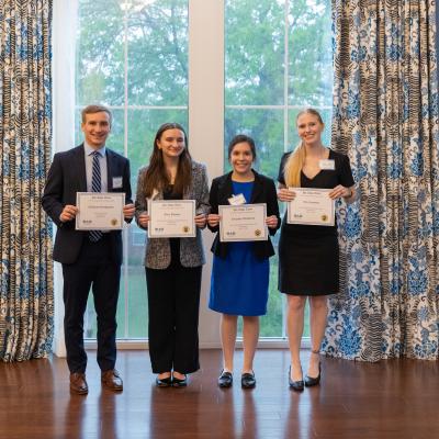 4 people stood in front of a bright window holding up awards in business professional clothing