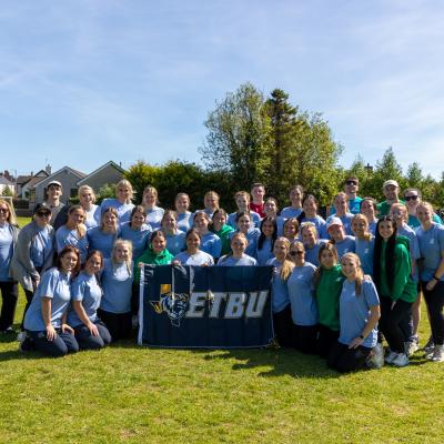 A large group of people standing outside in broad daylight with an ETBU banner in front of them