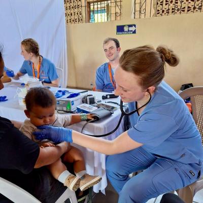 A woman tending to a pediatric patient wearing scrubs inside with a stethoscope