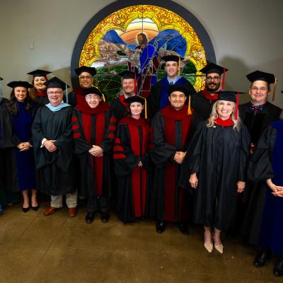 People standing inside in academic regalia infront of a stained glass window