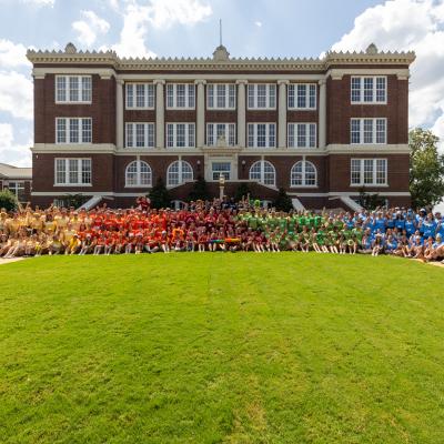 A group photo of a large group of student standing in front of a brick building