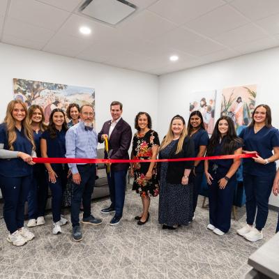 A group of people stood in a room with large scissors cutting a bright red ribbon