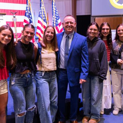 A group of people standing together smiling with the backdrop of American Flags on a stage