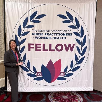 A woman in front of a backdrop sign that says the national association of nurse practitioners in womens health