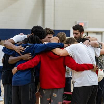 A group of men standing in a huddled circle praying