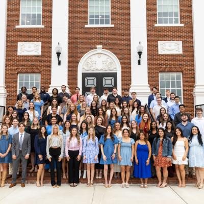 A group of people standing on the steps of a large brick building with white collumns