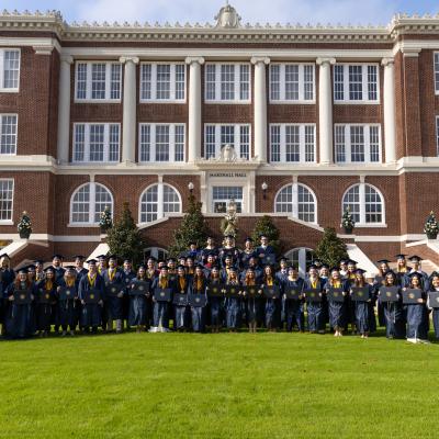 Group photo of graduates in navy regalia in front of Marshall Hall on a sunny day.