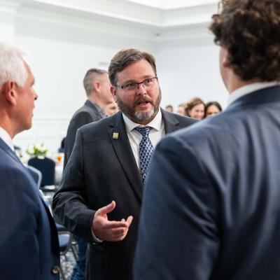 Men standing talking together in a crowded room wearing professional attire