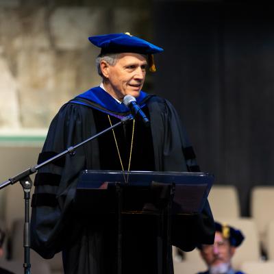 A man speaking behind a podium in academic regalia