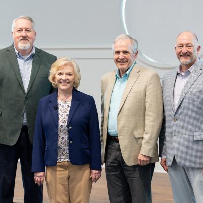 Four people stand together for a photo, each wearing a blazer and smiling