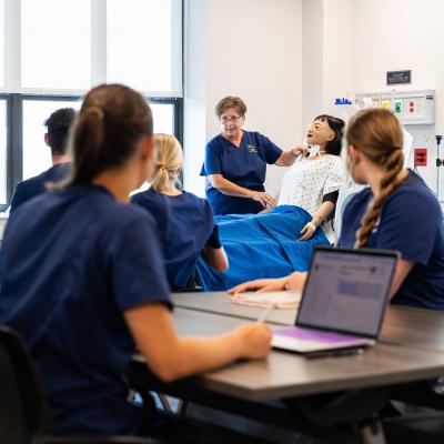 Nursing instructor with dummy teaches with students in the foreground.