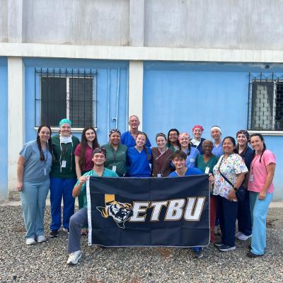 Group of people with an ETBU flag in front of a blue building.