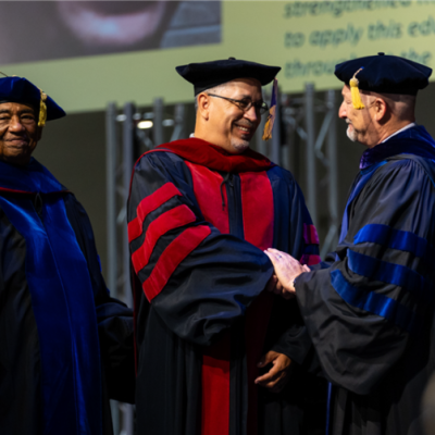 3 people standing inside in academic regalia shaking hands