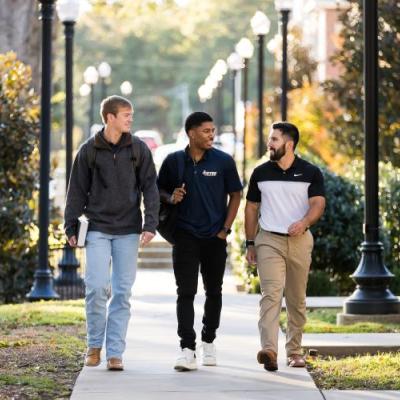 3 people walking and talking outside together on a narrow path