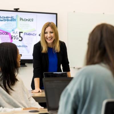 A female professor standing at the front of a classroom speaking to students.