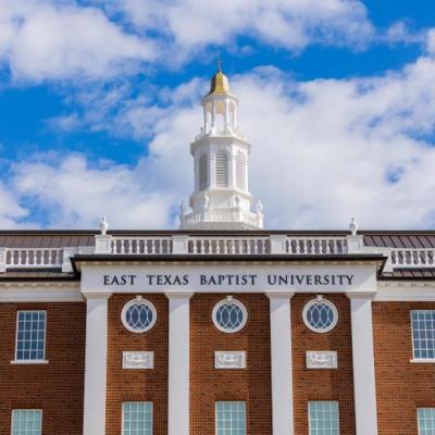 Brick building with white cupola with blue sky and white clouds 