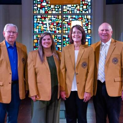 Four adults in golden blazers smiling at the camera