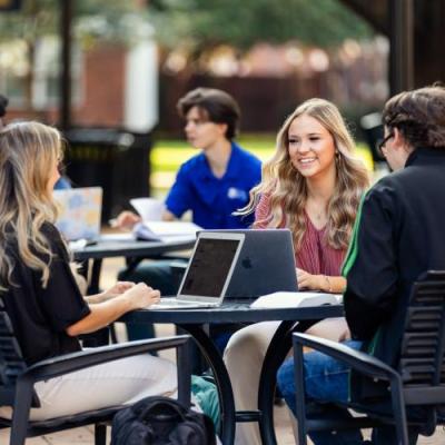 Students sitting at tables talking and studying with laptops and textbooks.