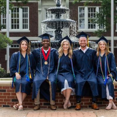 A group of people standing outside infront of a fountain in academic regalia