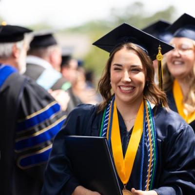 A woman in a navy cap and gown walking in a line of graduates.