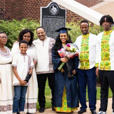 A large family smiling with a female graduate holding flowers in a navy cap and gown in the center.