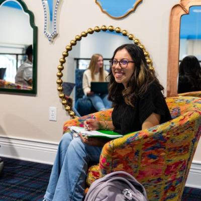 A woman sitting in a chair with long hair and glasses smiling