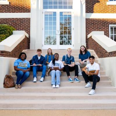 Seven students in shades of blue and white sitting on stairs outside of the red brick Marshall Hall.