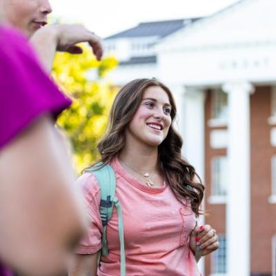 A girl smiling and talking to others in front of a red brick building with white columns.