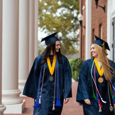 Two females in navy regalia walking on a red brick building porch.