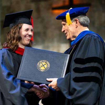 A man and woman wearing academic regalia holding a diploma