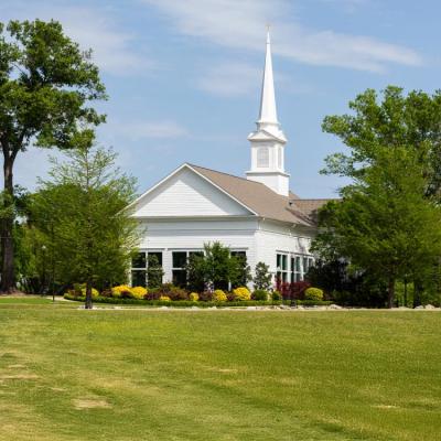 White chapel with steeple among greenery and a blue sky and clouds.