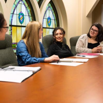 People sitting at a table inside with books on a desk infront of stained glass windows