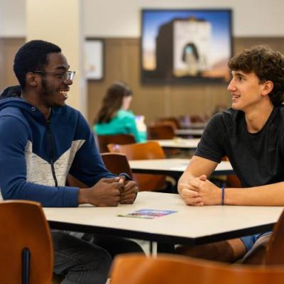 2 men sitting at a table talking to eachother inside
