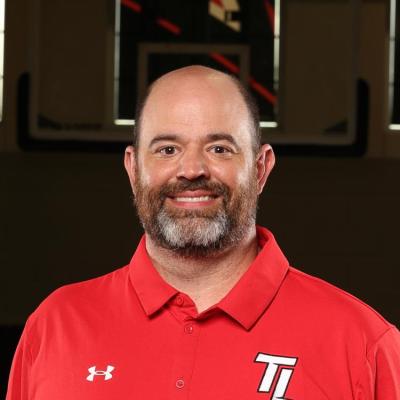 A man in athletic attire stood smiling in fron tof a basketball goal