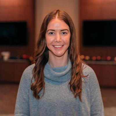 A woman posing inside in front of a dark backdrop with televisions